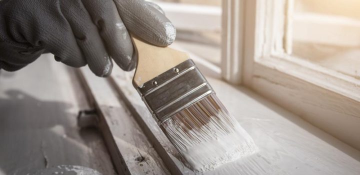 Painting wooden window with white color. Brush in hand with grey