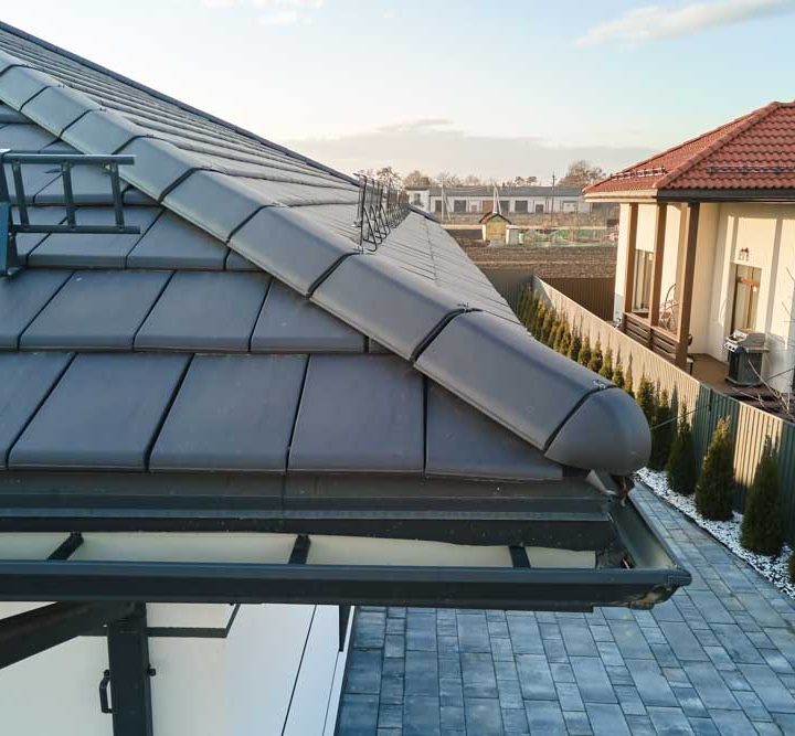 Closeup of house roof top covered with ceramic shingles with gutter pipes for rain water. Tiled covering of building